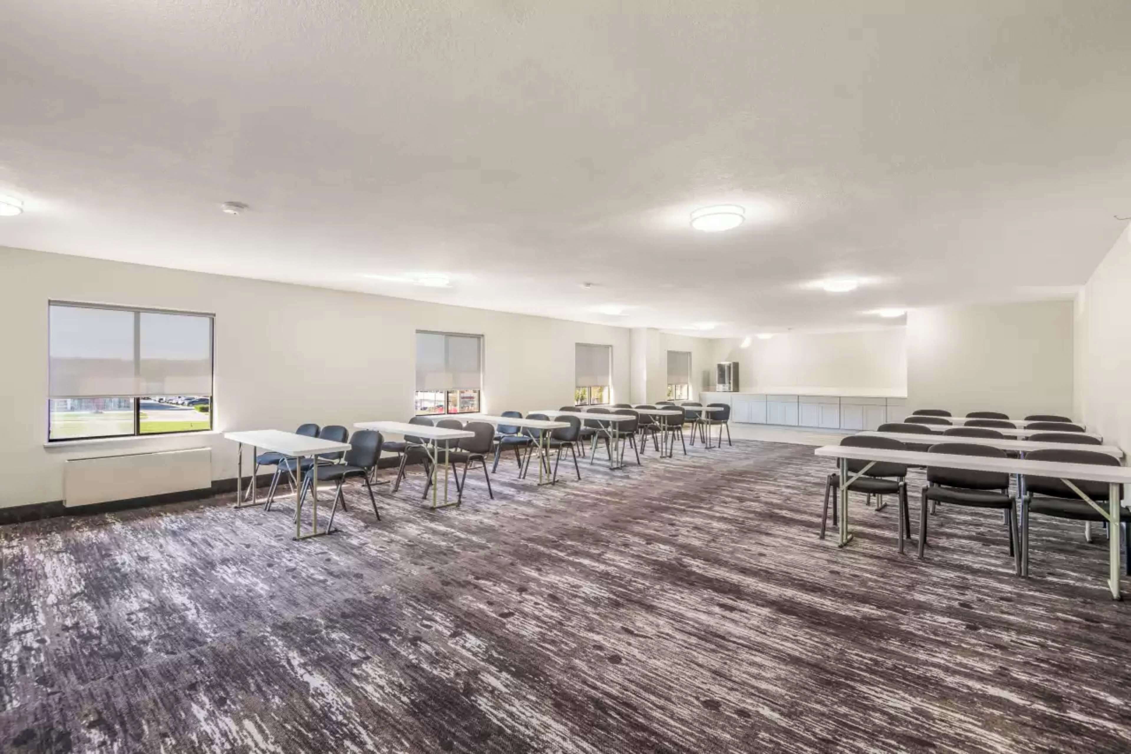 A conference room with multiple tables and chairs, large windows, and a carpeted floor.