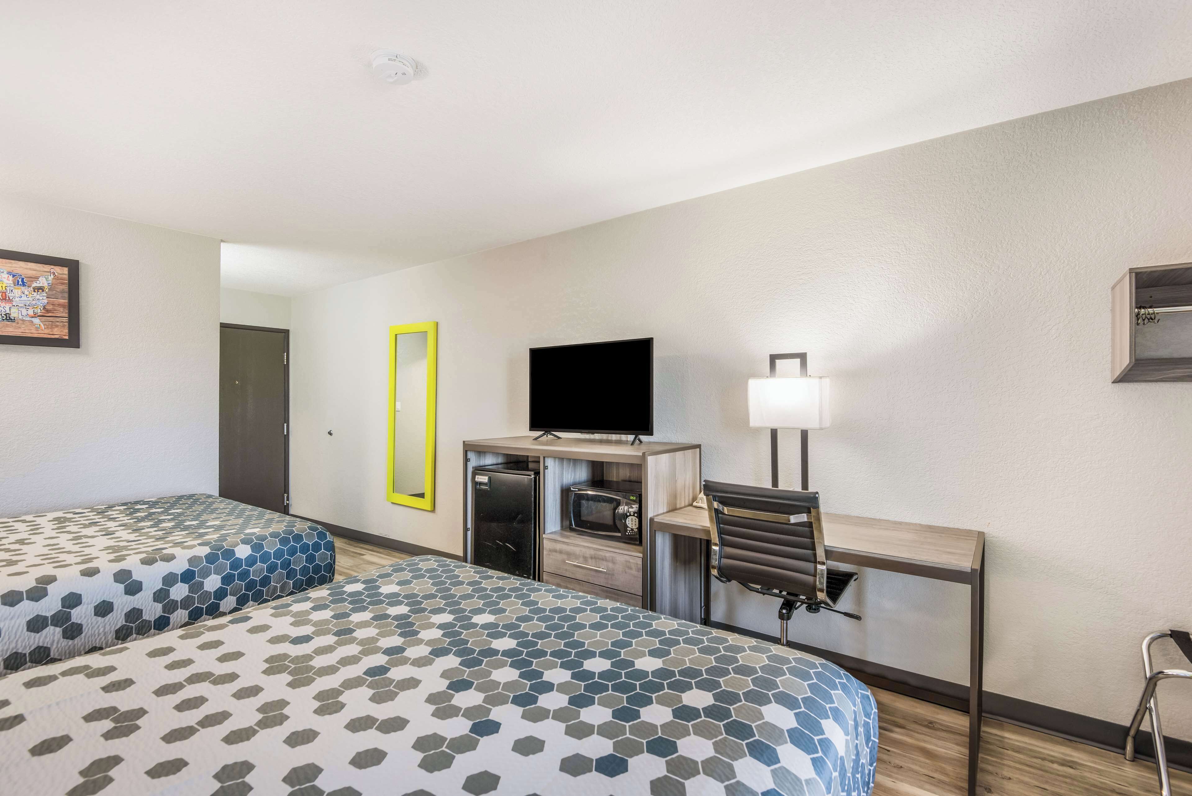 A hotel room with two beds, a desk with a computer, a television, and a lamp.