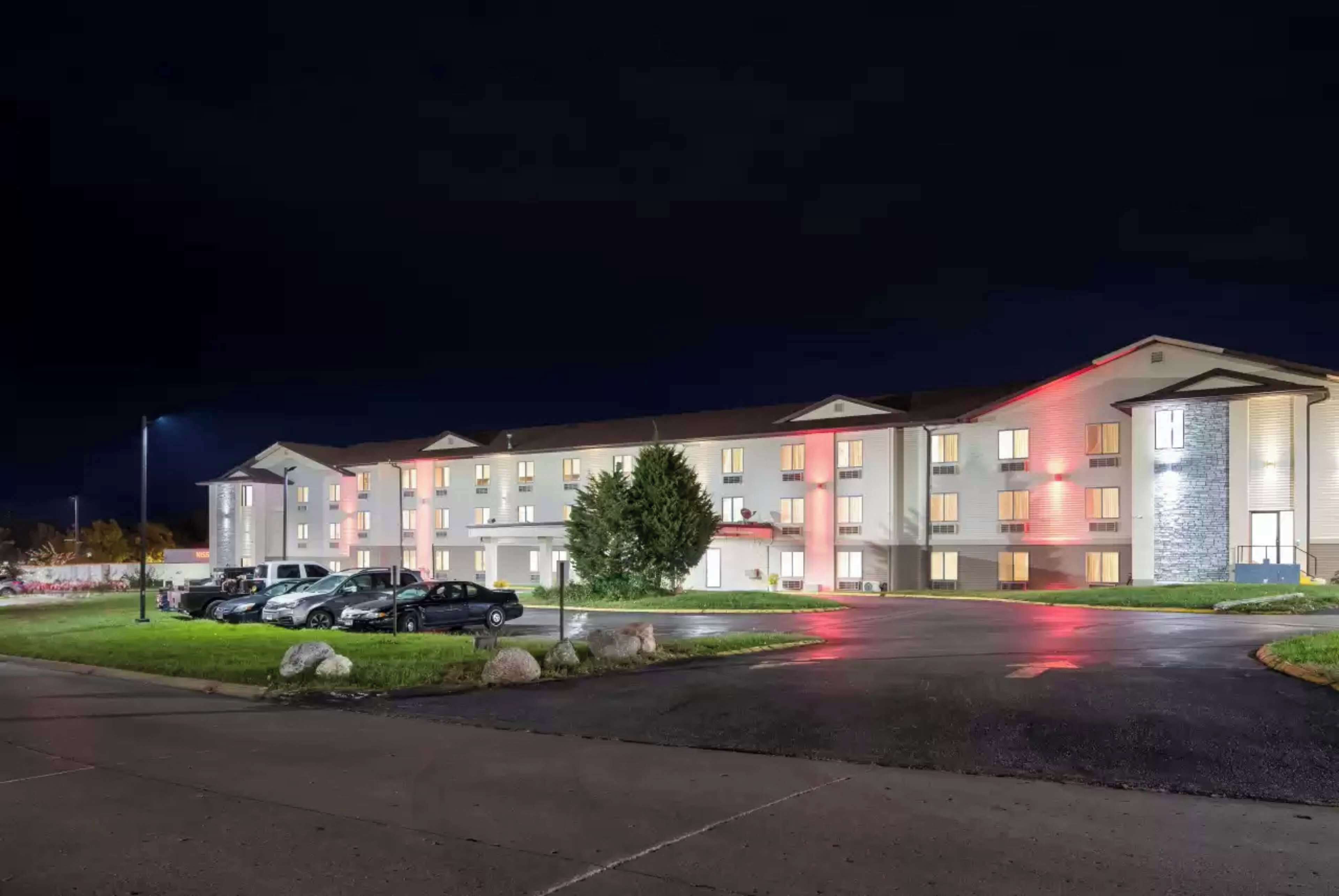 Un hôtel à plusieurs étages, doté d’un parking et d’une façade bien éclairée.