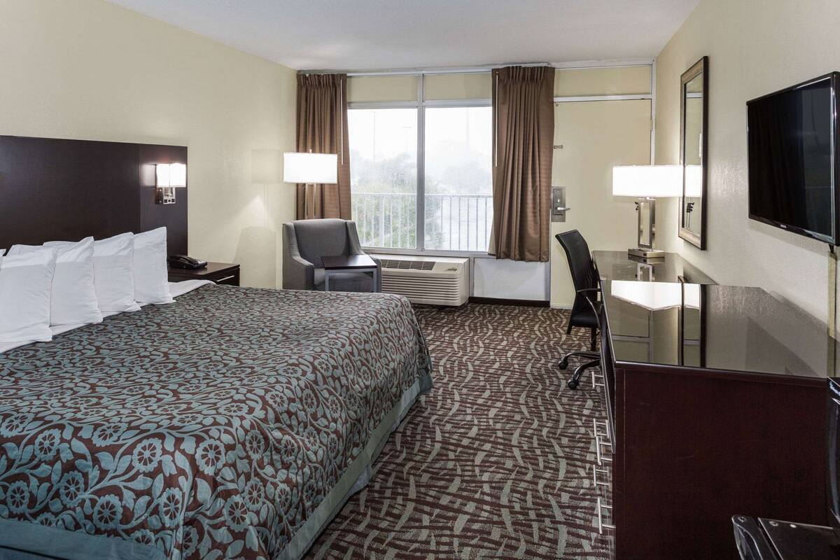 A hotel room with a large bed, a desk, a chair, a TV, and a window with curtains.