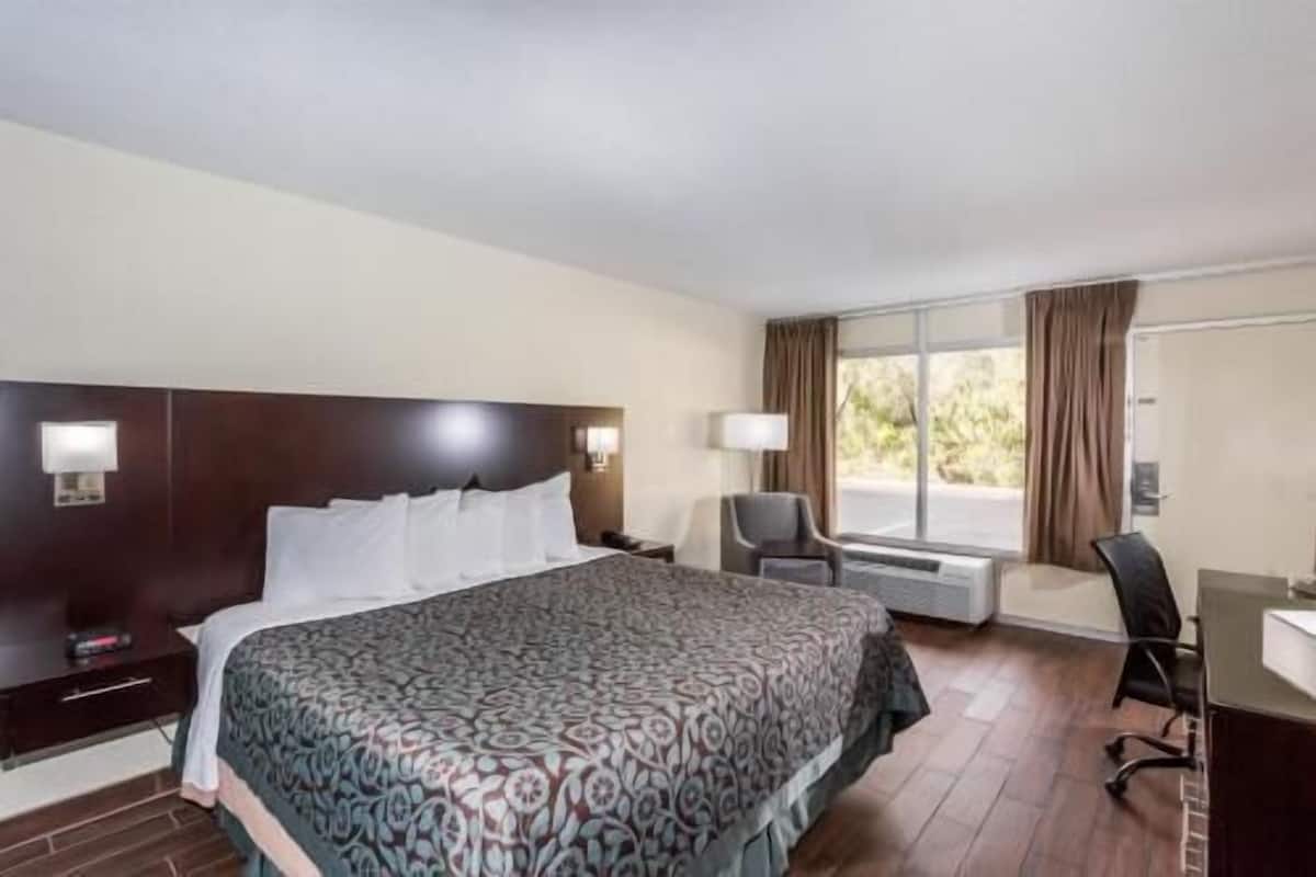 A hotel room with a large bed, a desk, a chair, and a window with curtains.