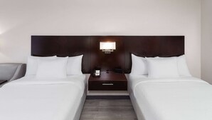 Quarto de hotel com duas camas, uma mesa de cabeceira com abajur e uma gaveta pequena.
