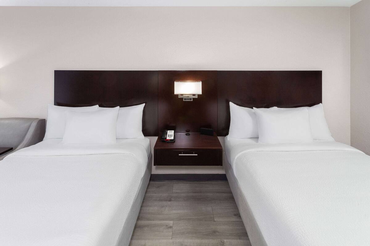 A hotel room with two beds, a nightstand with a lamp, and a small drawer.
