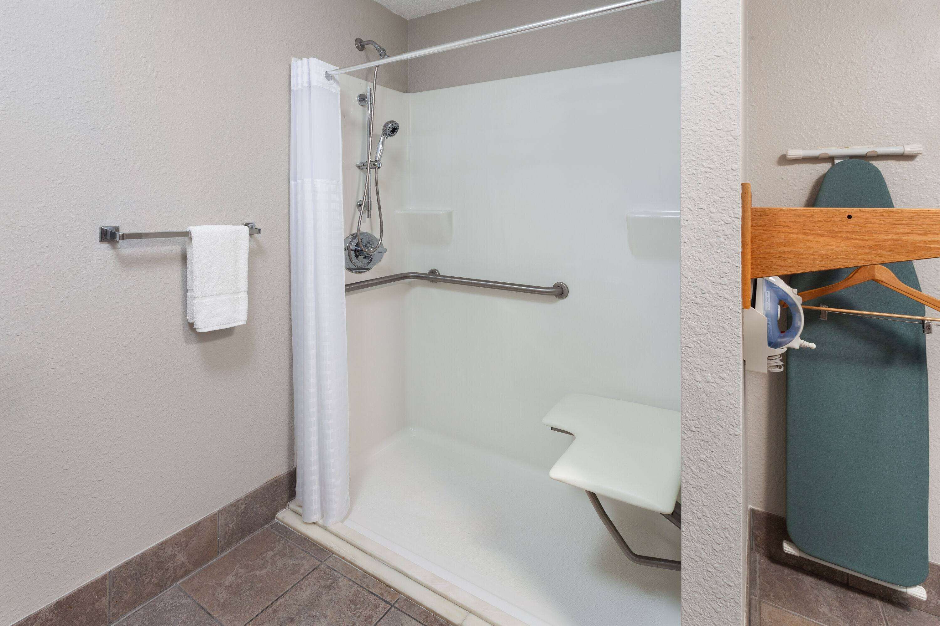 A shower area with a glass door, a white towel rack, a grab bar, and a small shelf.