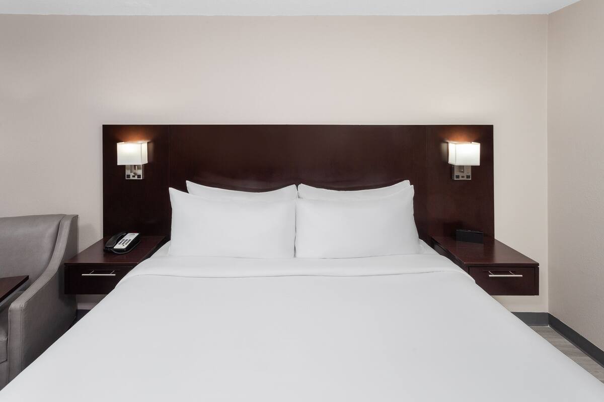 A hotel room with a large bed, two bedside tables, a nightstand, a telephone, and two wall-mounted lamps.