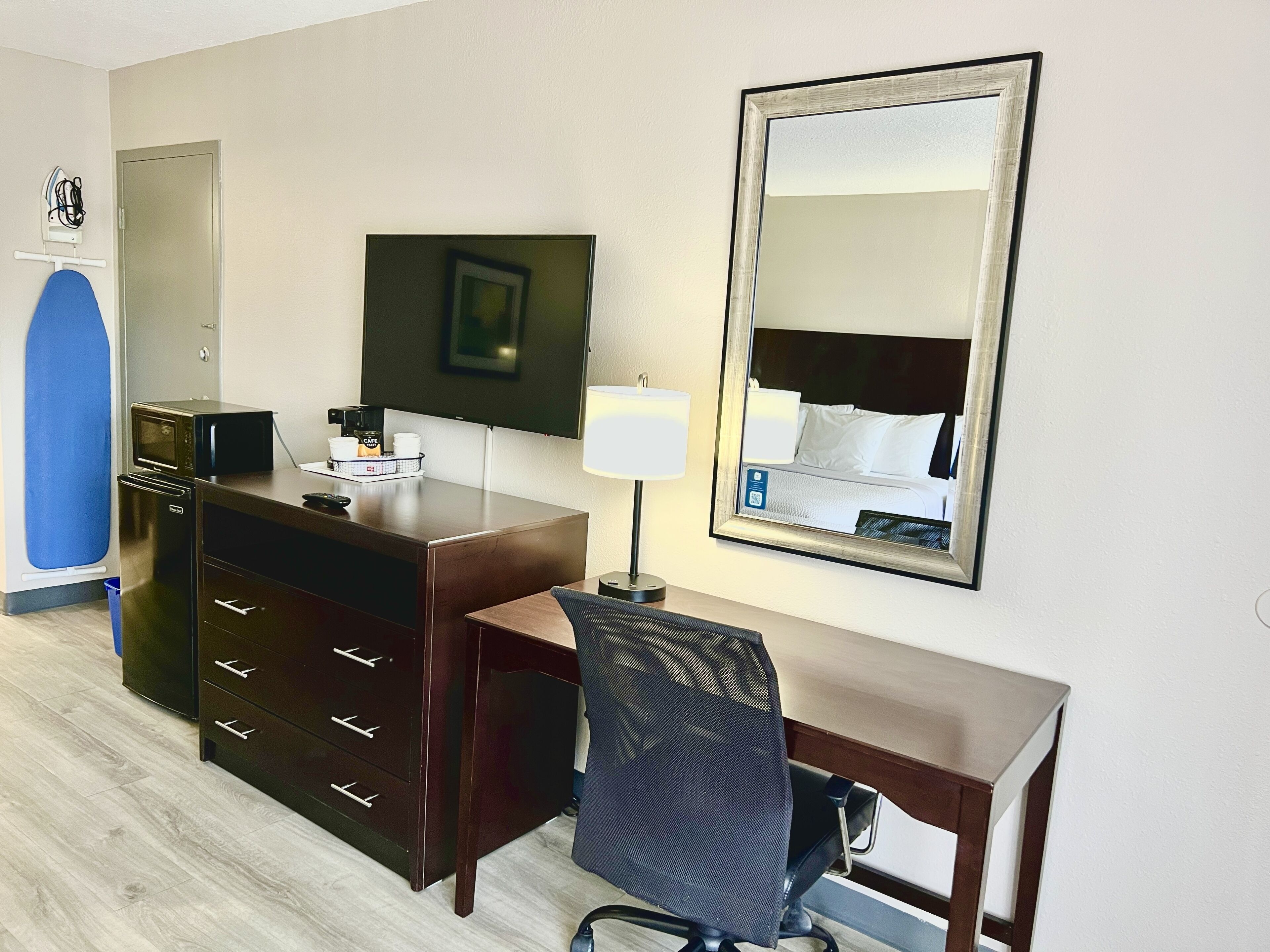 Habitación de hotel con escritorio, silla, televisor y un espejo grande.