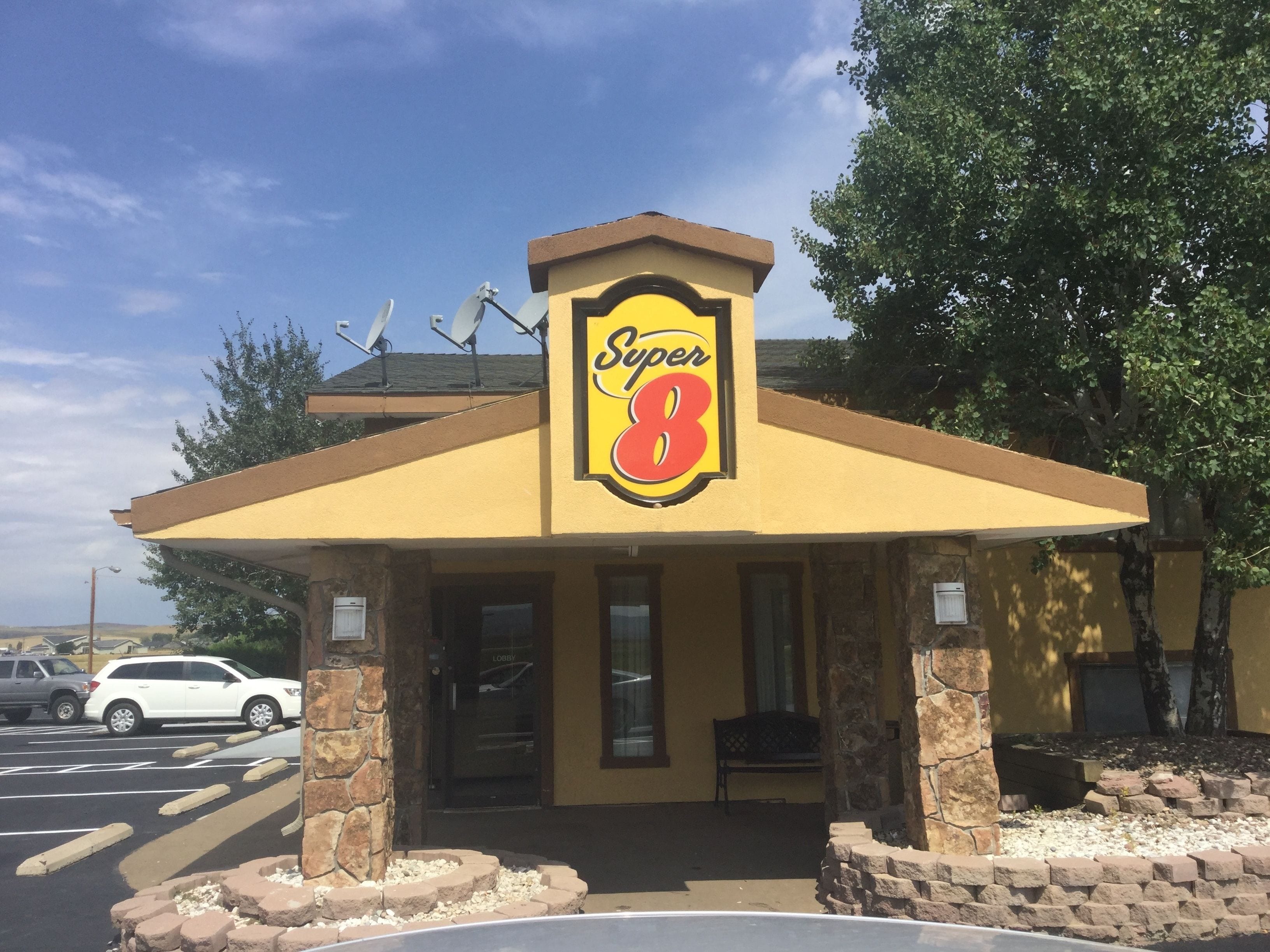 A Super 8 motel with a yellow facade, stone pillars, and a clear sky in the background.