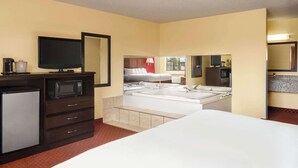Une chambre d’hôtel comprenant un lit, une télévision, un four à micro-ondes, un réfrigérateur, une salle de bain avec une baignoire et un lavabo, ainsi qu’un miroir.