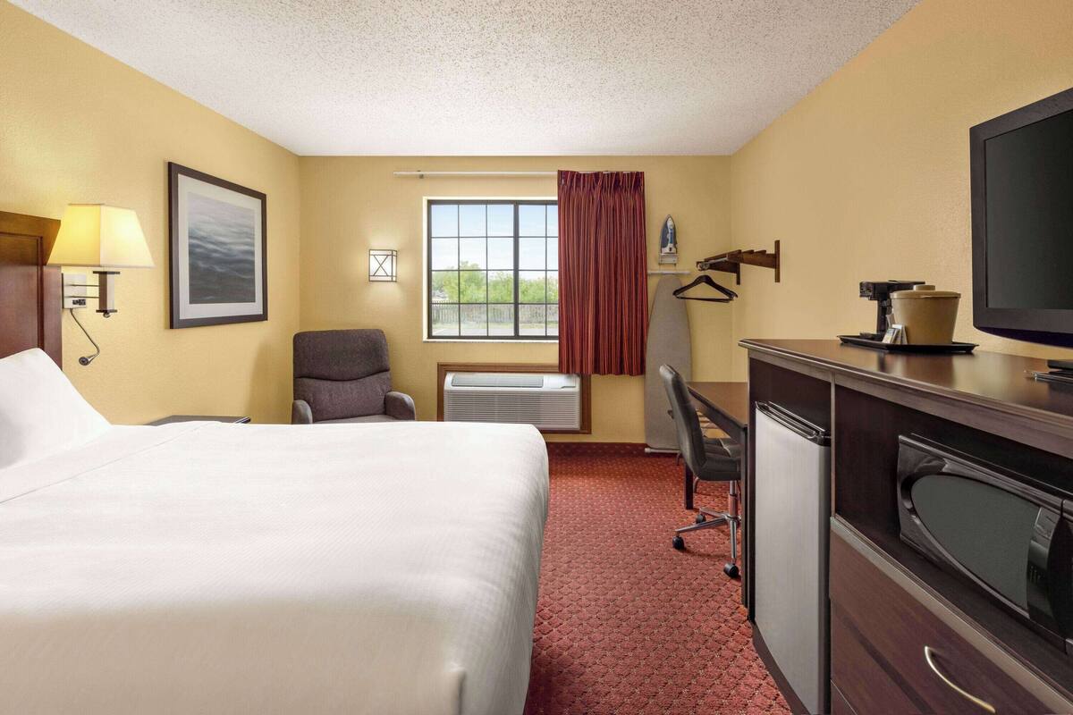 A hotel room with a bed, desk, chair, TV, and a window with curtains.