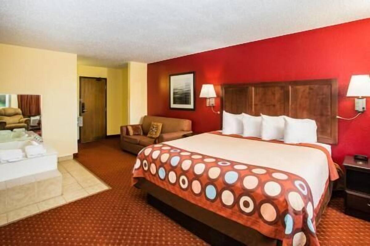 A hotel room with a large bed, a sofa, a desk, and a bathroom.