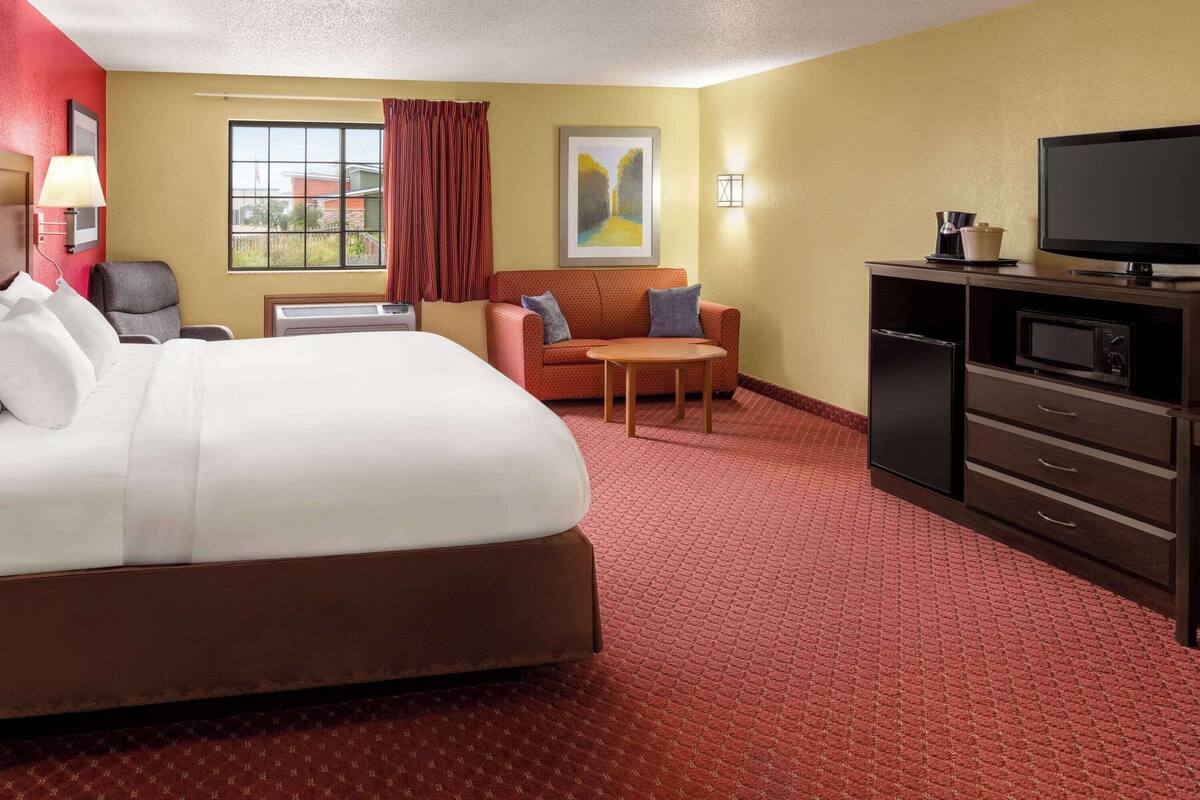 A hotel room with a large bed, a sofa, a small table, a TV, a microwave, and a desk with a lamp.