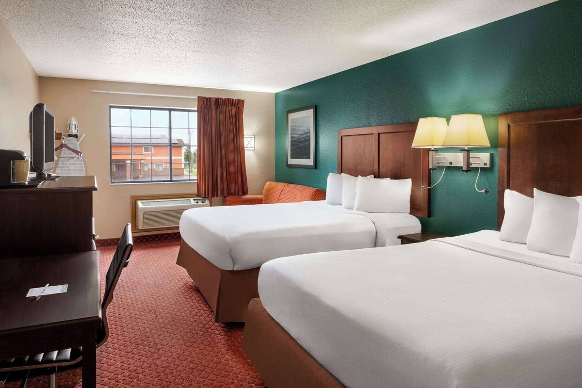A hotel room with two beds, a desk, a chair, a TV, and a window with curtains.