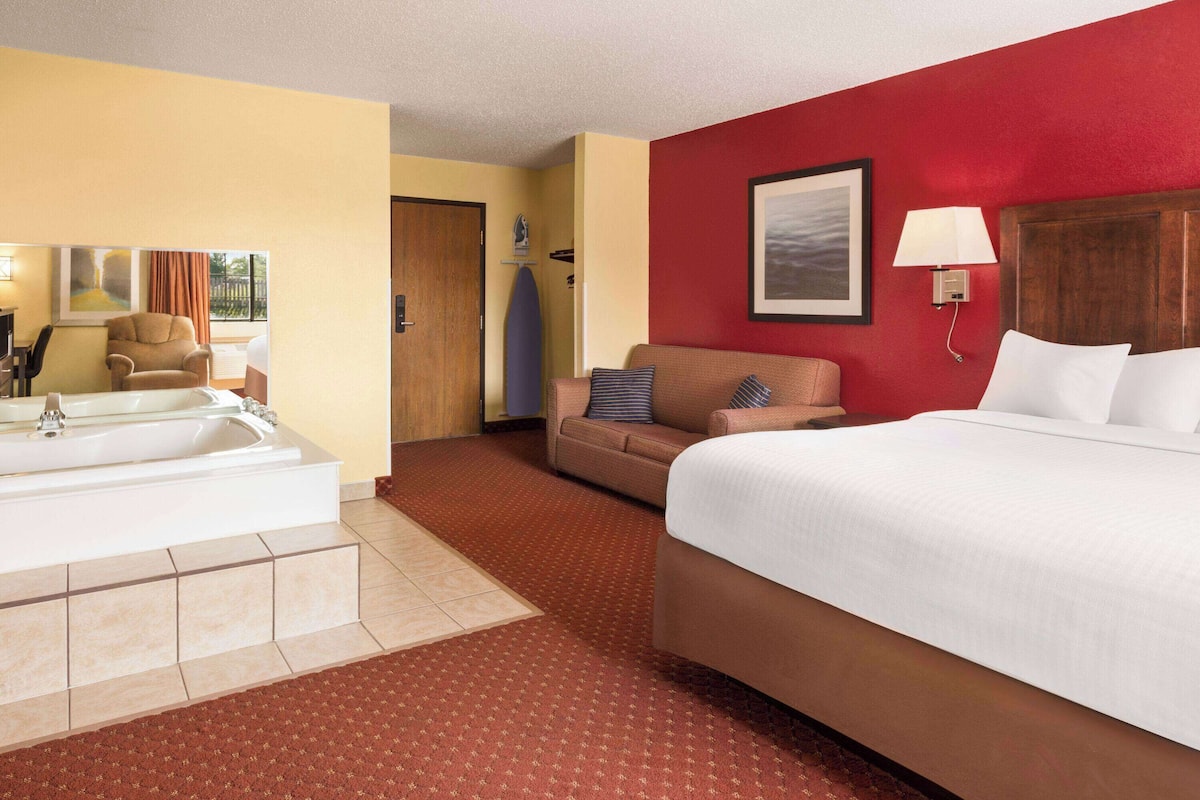 Une chambre d’hôtel avec un grand lit, un canapé, un fauteuil, une baignoire et un mur d’accent de couleur rouge.