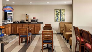 Un espace réservé au petit-déjeuner, avec des chaises en bois, un four à micro-ondes, une machine à café et un panneau indiquant l’emplacement du coin petit-déjeuner.