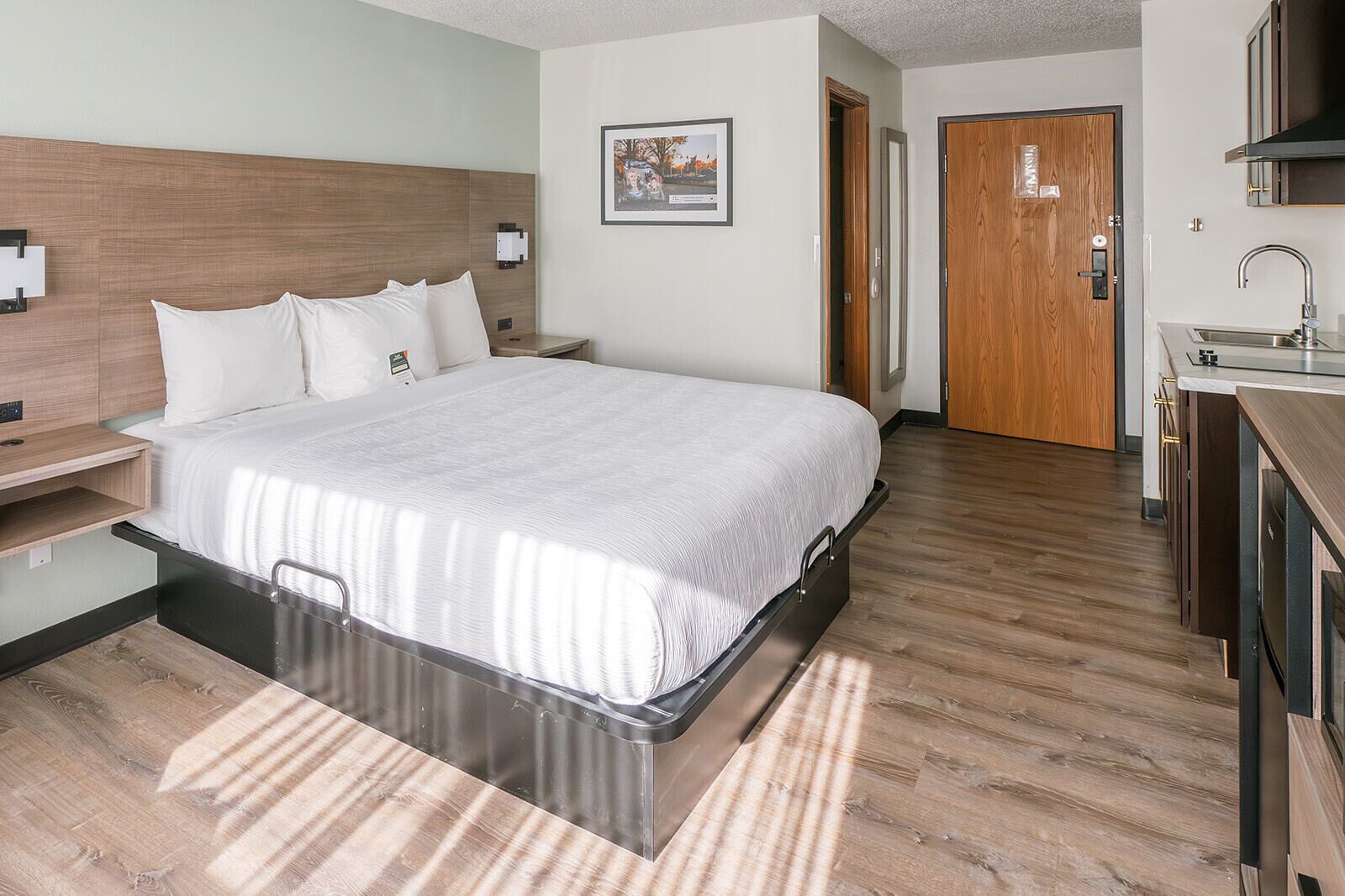 Habitación de hotel con cama, mesita de noche y vistas al pasillo y al baño.