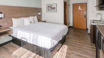 Habitación de hotel con cama, mesita de noche y vistas al pasillo y al baño.