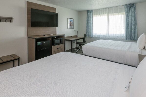 Habitación de hotel con dos camas, un televisor de pantalla plana, un escritorio con una silla, un microondas y un refrigerador pequeño.