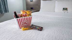 A bed with white bedding, a pop corn container, and two candy bars.