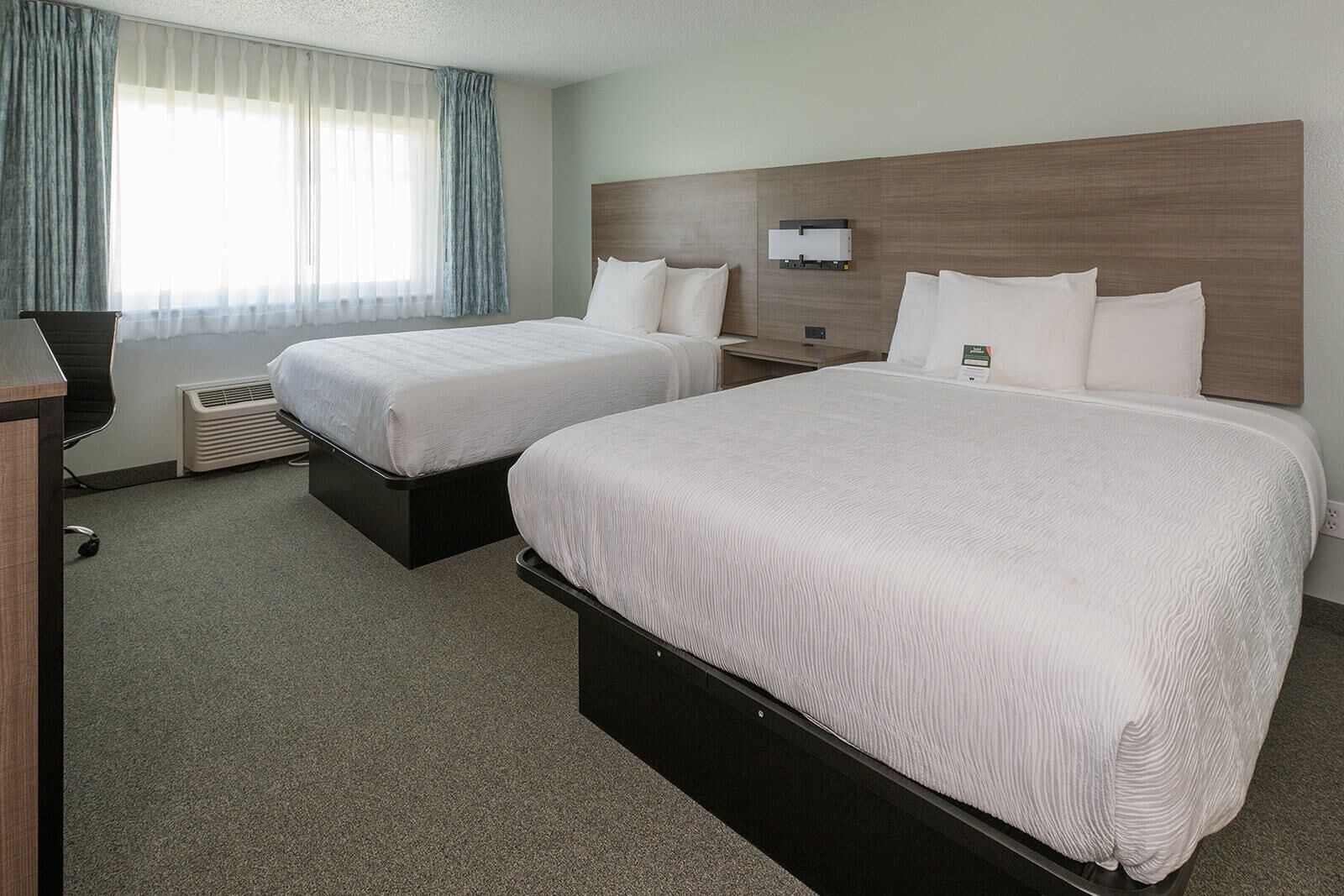 Habitación de hotel con dos camas, un escritorio, una silla y una ventana con cortinas.