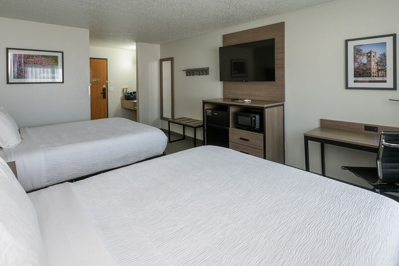 Ein Hotelzimmer mit zwei Betten, einer Mikrowelle, einem kleinen Schreibtisch und einem Fernseher.