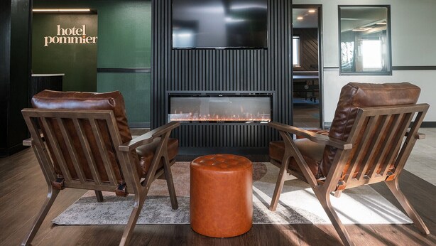 A modern hotel lobby with leather armchairs, a central fire feature, and a large TV screen.