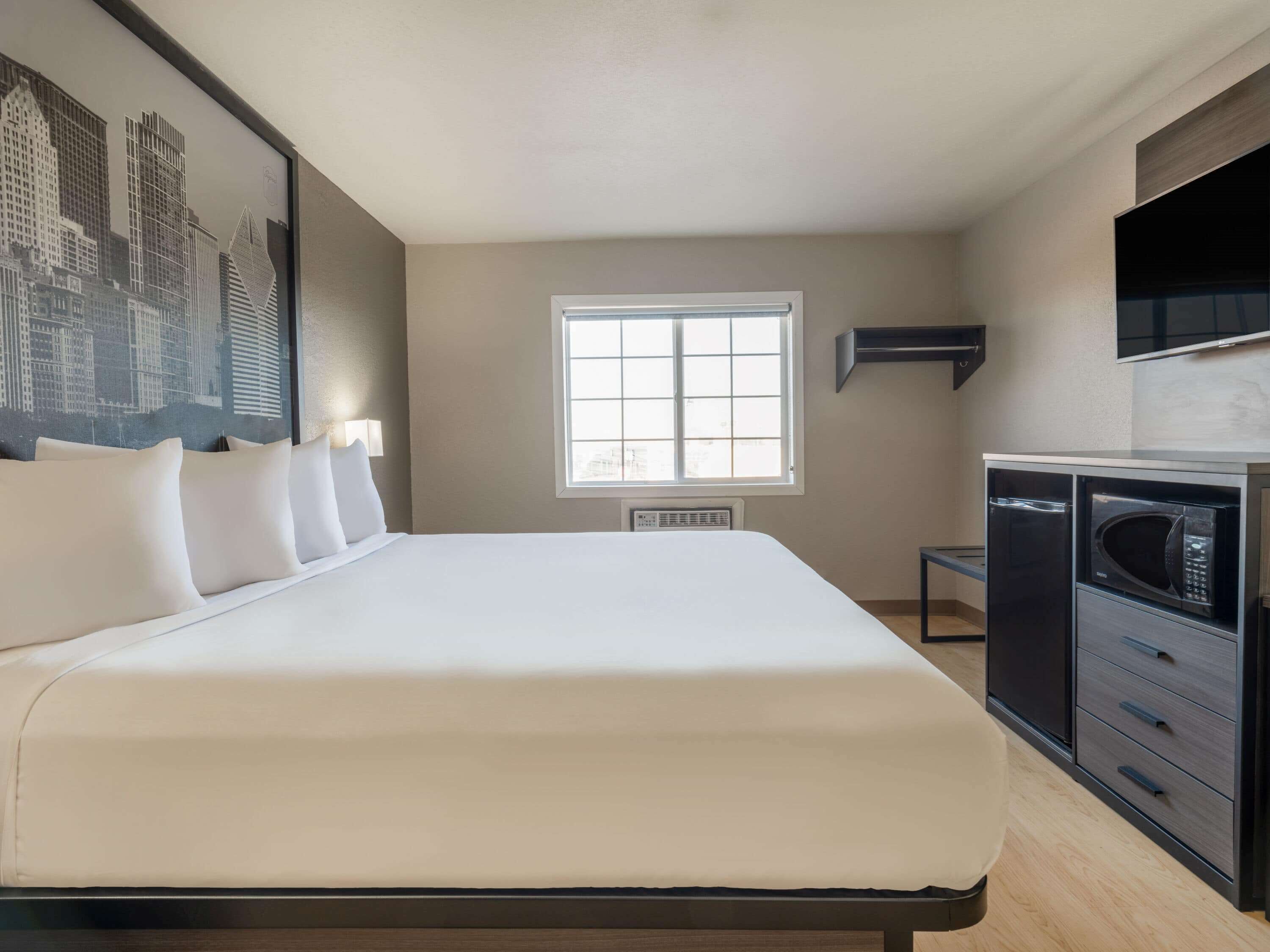 A hotel room with a large bed, a window, a flat-screen TV, a microwave, and a small table.