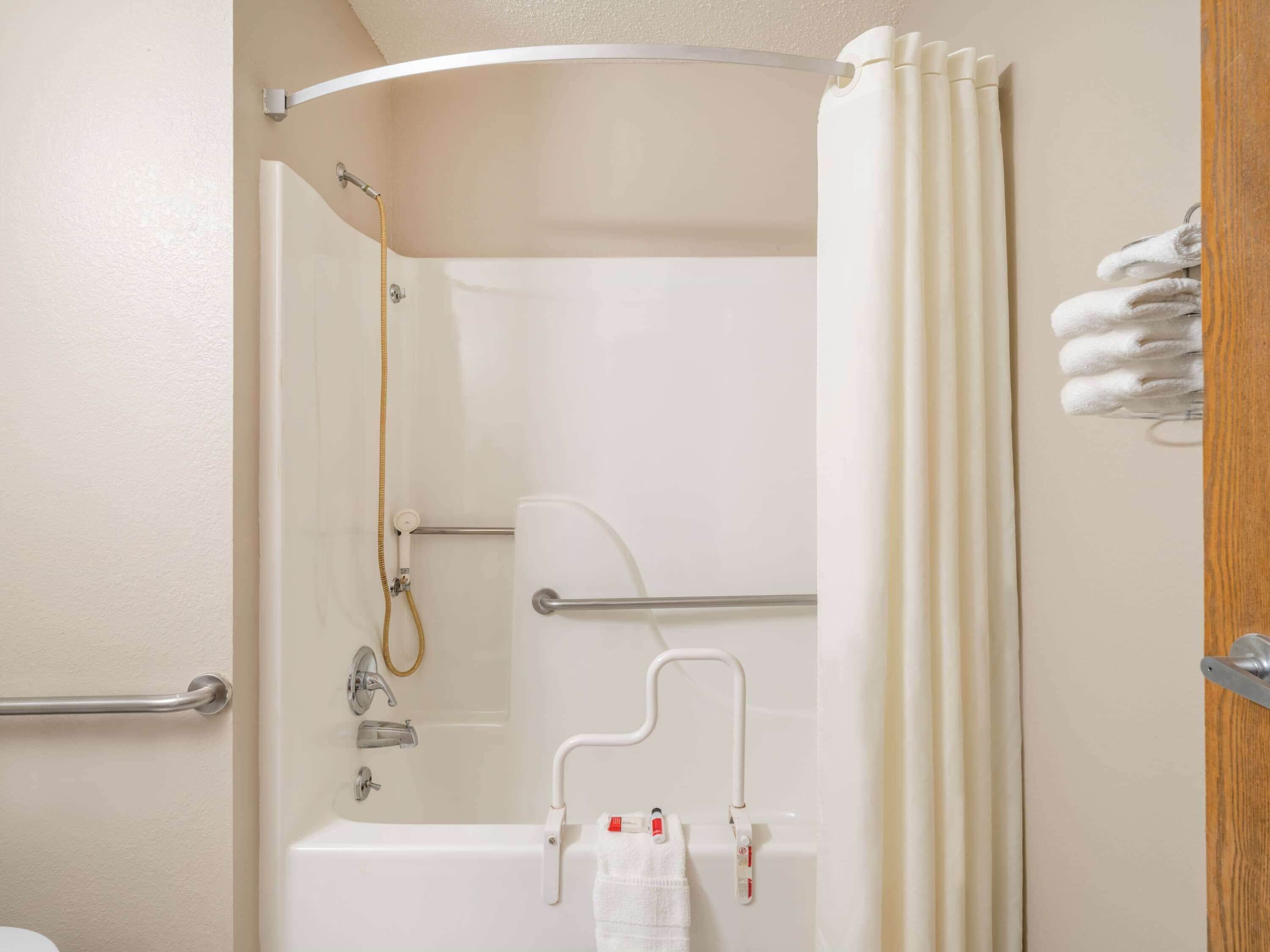 Un baño con bañera, ducha e inodoro. Hay barras de apoyo, un perchero para toallas y una cortina de ducha.