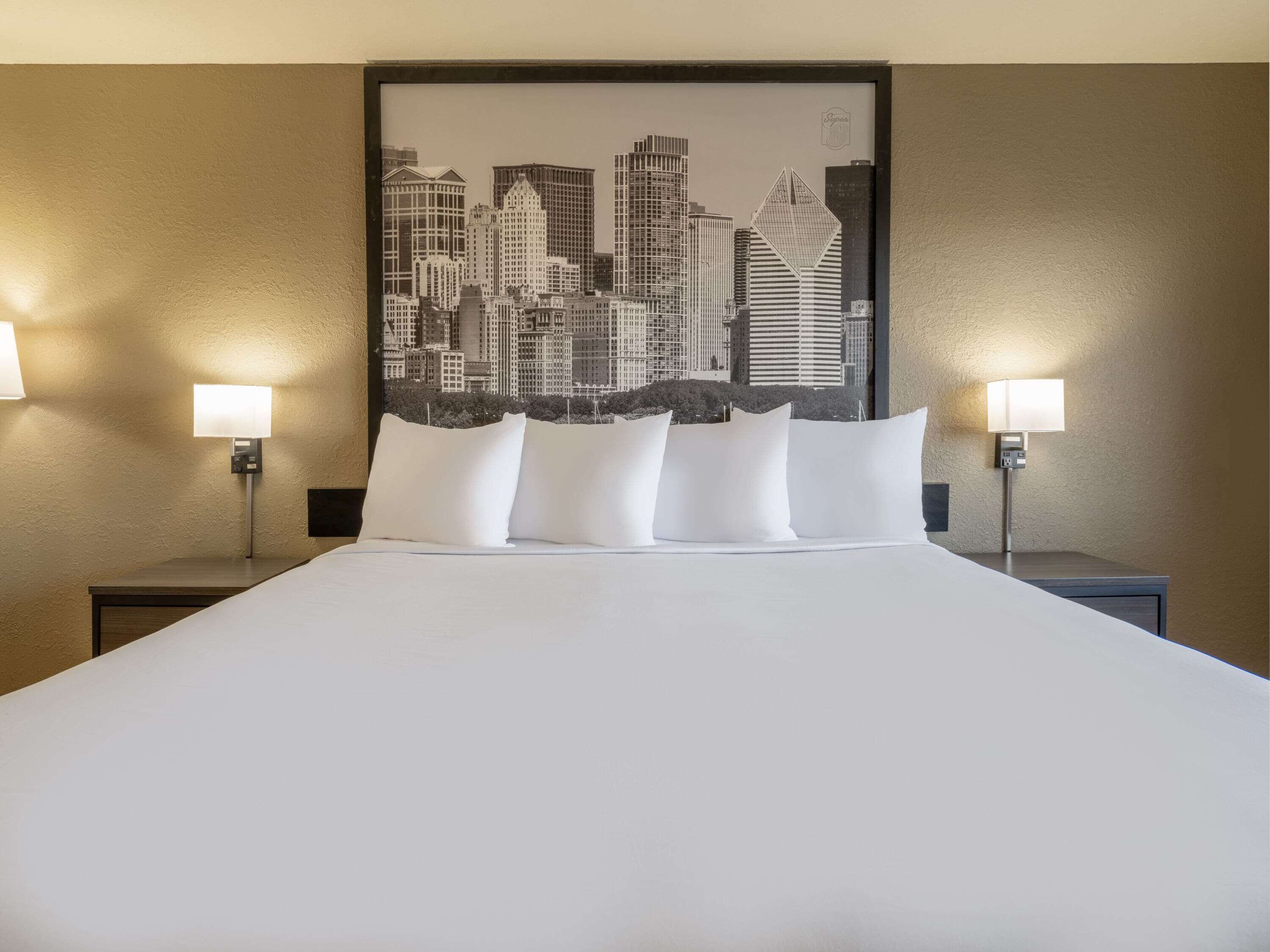 Habitación de hotel con una cama grande, dos mesitas de noche y vistas a la ciudad.
