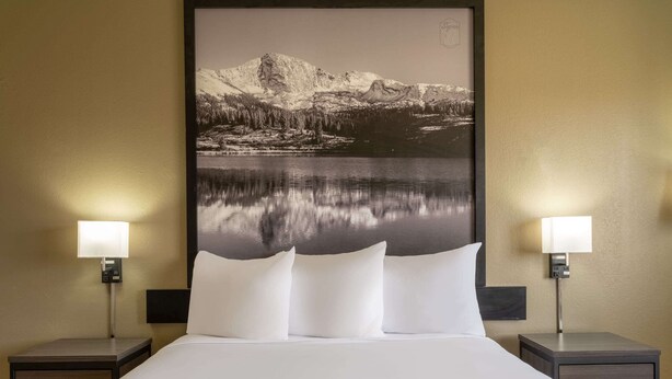 A hotel room with a large bed, two bedside tables with lamps, and a large framed picture of a mountain landscape on the wall. - Super 8 by Wyndham Clinton (Clinton)