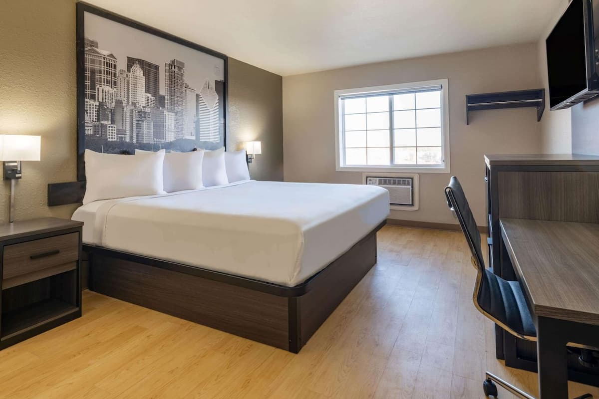 A hotel room with a large bed, a desk, a chair, a TV, a window, and a cityscape view.