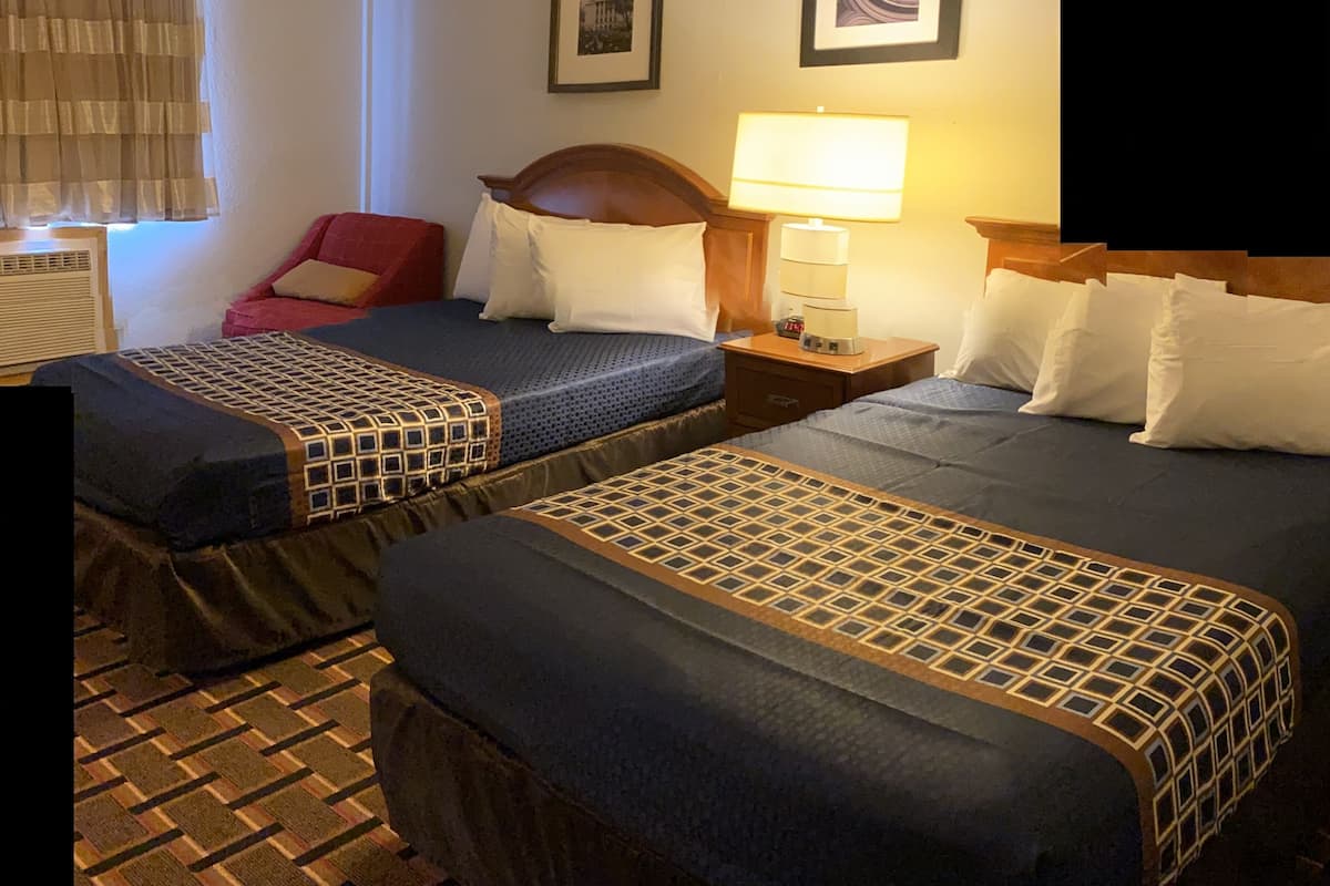 A hotel room with two beds, a red chair, a nightstand with a lamp, and two framed pictures on the wall.