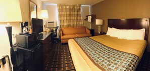A hotel room with a bed, a sofa, a desk with a computer, a TV, and a coffee maker. - Le Mars Inn & Suites (Le Mars)