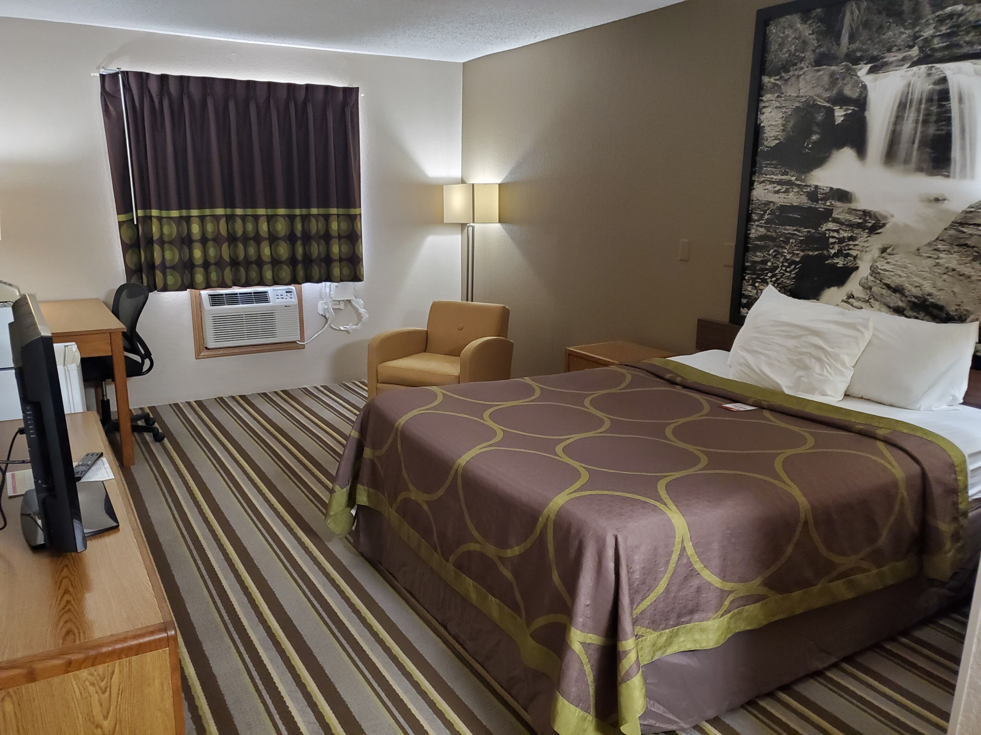 Une chambre d’hôtel équipée d’un lit, d’un bureau, d’un climatiseur, d’une chaise et d’une lampe fixée au mur.