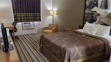 Une chambre d’hôtel équipée d’un lit, d’un bureau, d’un climatiseur, d’une chaise et d’une lampe fixée au mur.