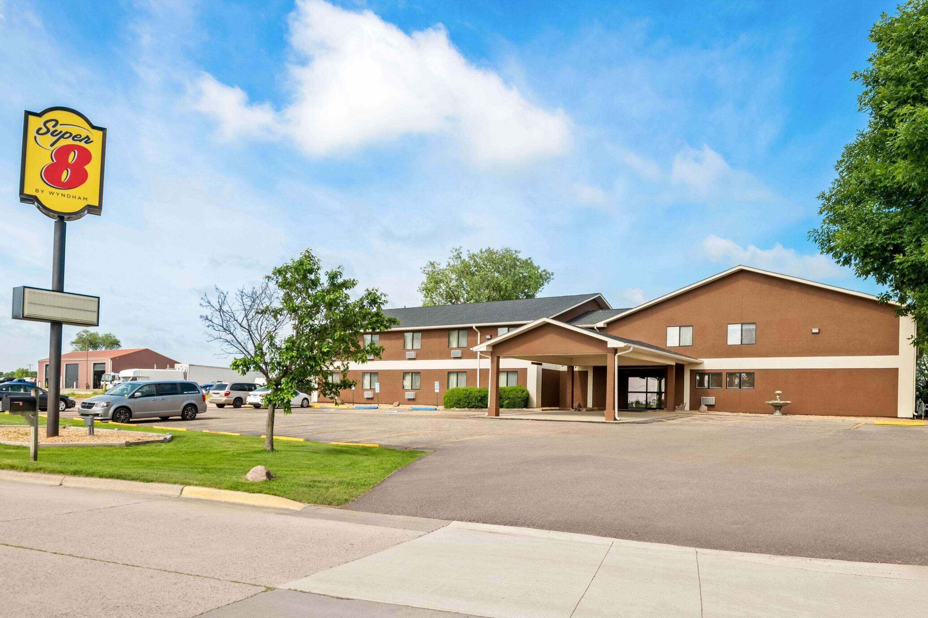 A Super 8 hotel with a parking lot, a covered parking area, and a building with multiple windows and a flat roof.
