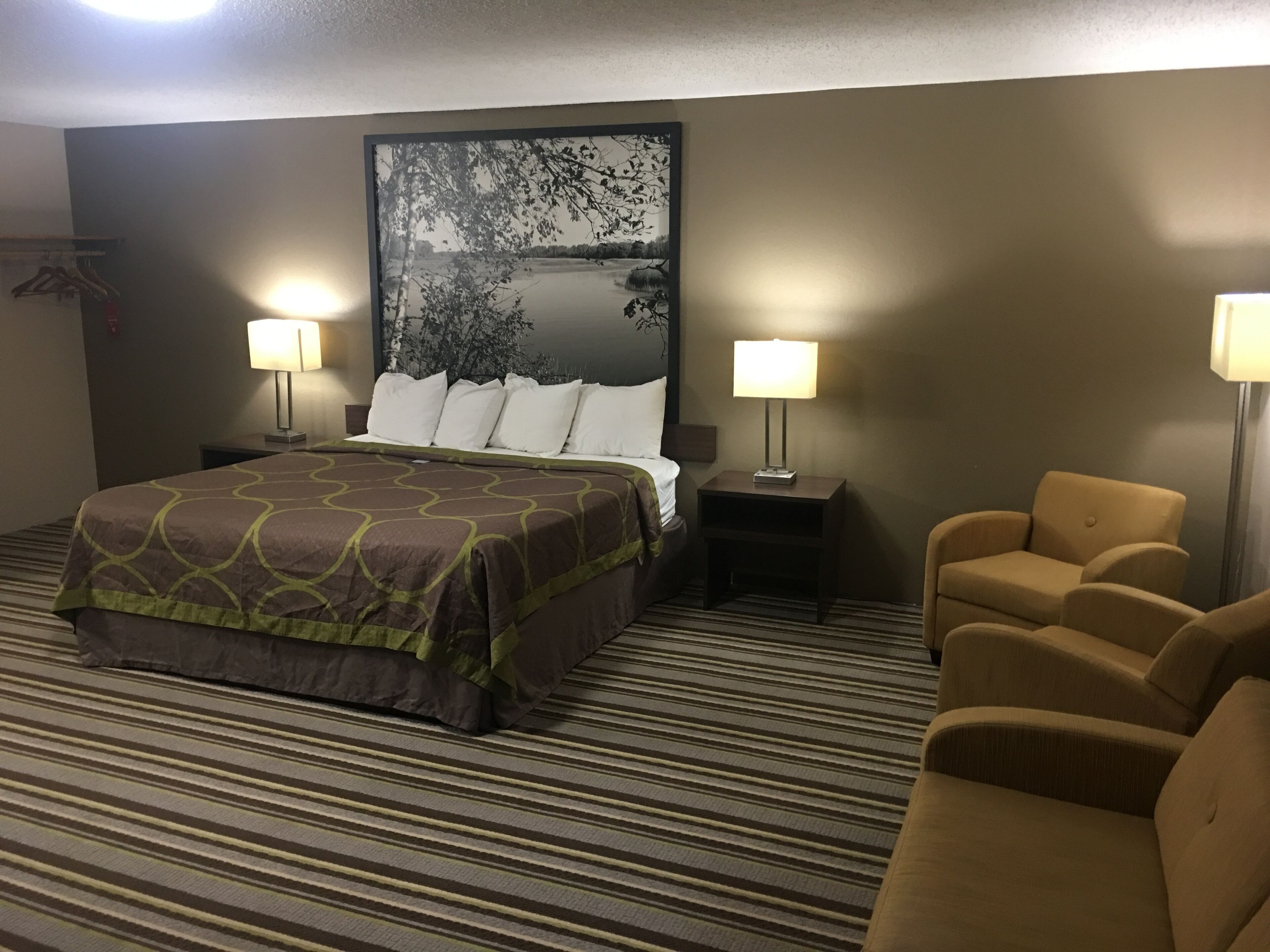 Una habitación de hotel con una cama grande, dos lámparas de noche, una silla y un cuadro en la pared.