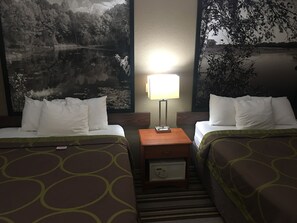 Two single beds with white linens and brown bedspreads, a black and white landscape painting, and a simple nightstand with a lamp.