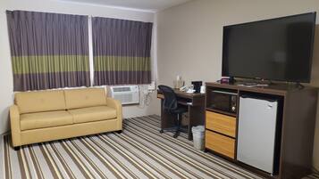 A hotel room with a sofa, a desk with a computer, a television, and a minibar.