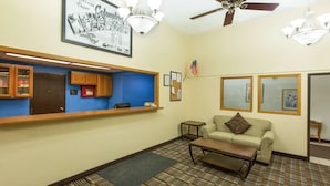 A hotel lobby with a reception desk, a sofa, a coffee table, patterned carpet, and a ceiling fan. - Super 8 by Wyndham Columbus (Columbus)