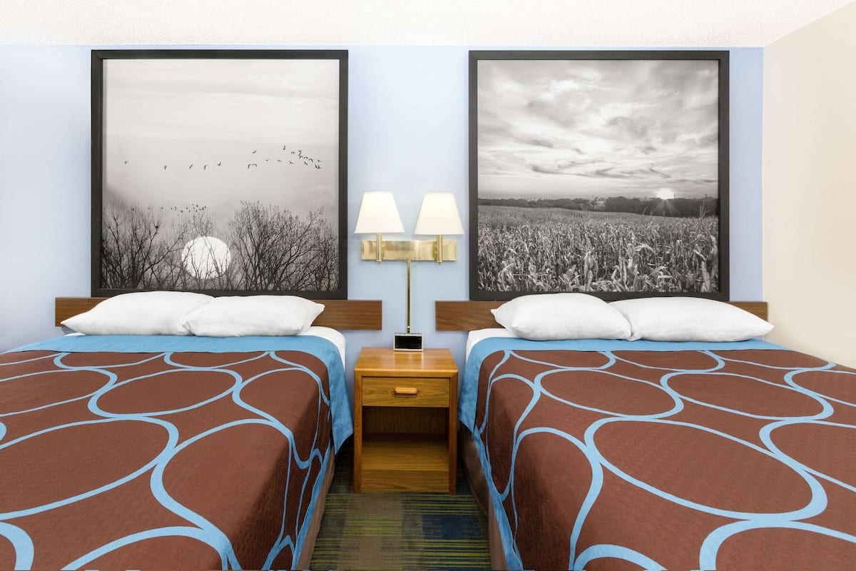 A hotel room with two beds, each with a patterned bedspread, a nightstand with a lamp, and two framed pictures on the wall.