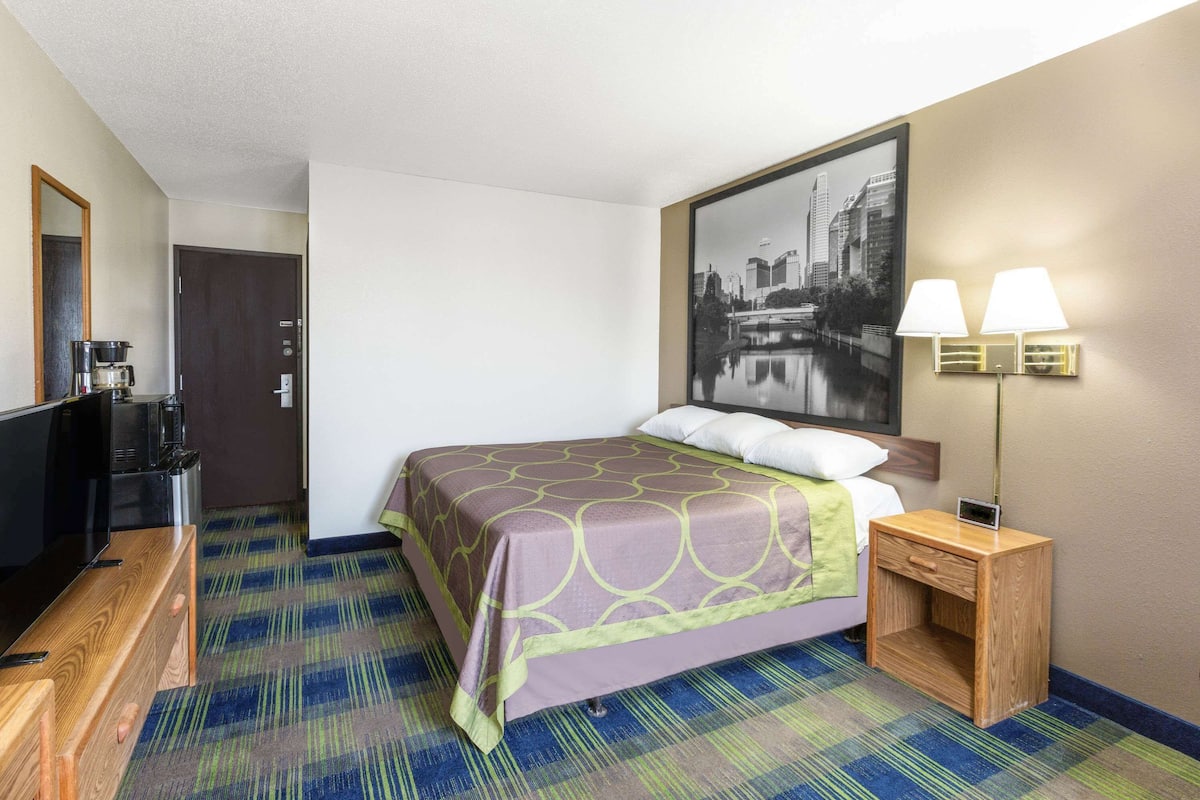 A hotel room with a bed, a bedside table with a lamp, a television, and a coffee maker.