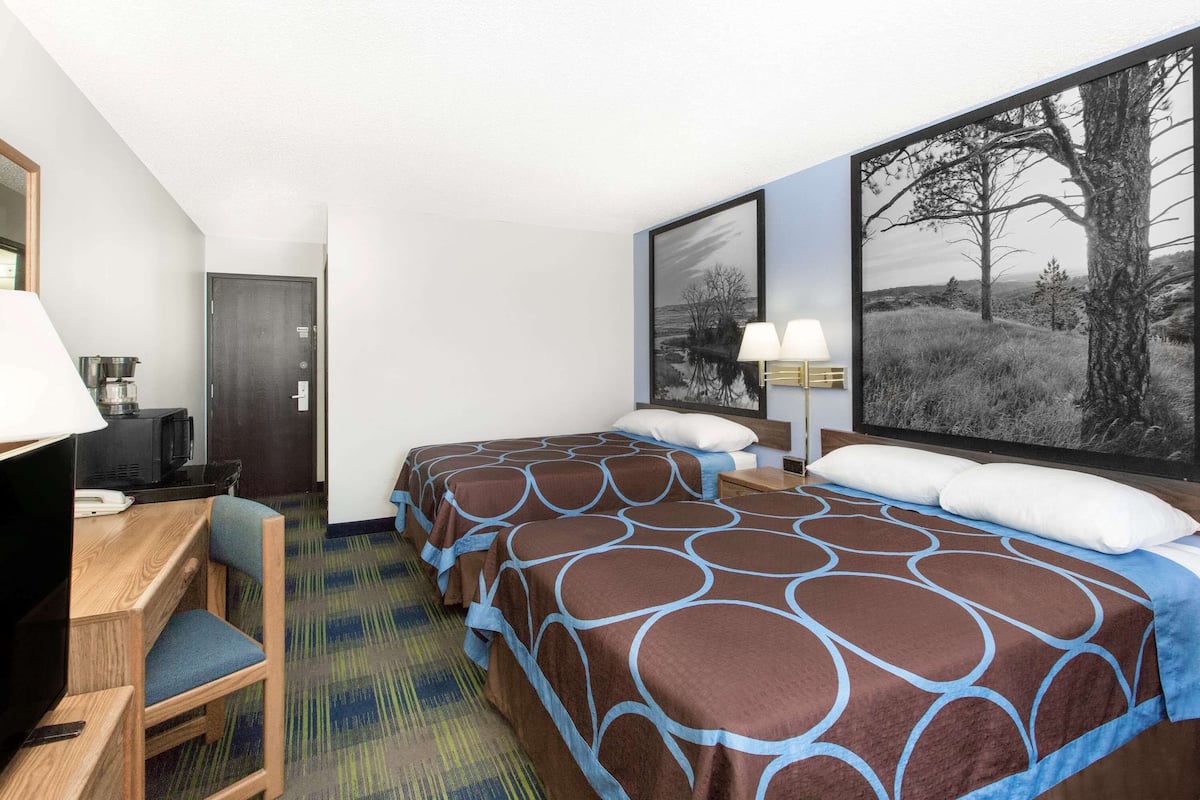 A hotel room with two beds, a desk with a chair, a television, and a large window with a landscape view.