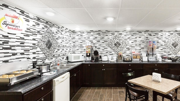 A modern kitchen with a breakfast bar, dark wood cabinets, a tiled backsplash, and a dining area with a table and chairs. - Super 8 by Wyndham Columbus (Columbus)