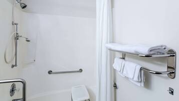 A bathroom with a shower, grab bars, a white towel rack, and a small white stool.