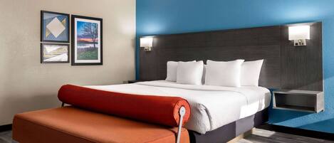 A modern hotel room with a bed, a red bench, and artwork on the wall.