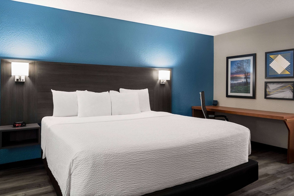 Una habitación de hotel con una cama grande, dos mesitas de noche, un escritorio y una silla.