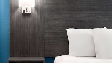 A hotel room with a dark wood headboard, a bedside table, and a white bed with pillows.