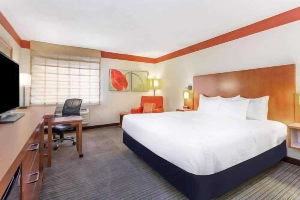 Habitación de hotel con cama, escritorio, silla y ventana con persianas.