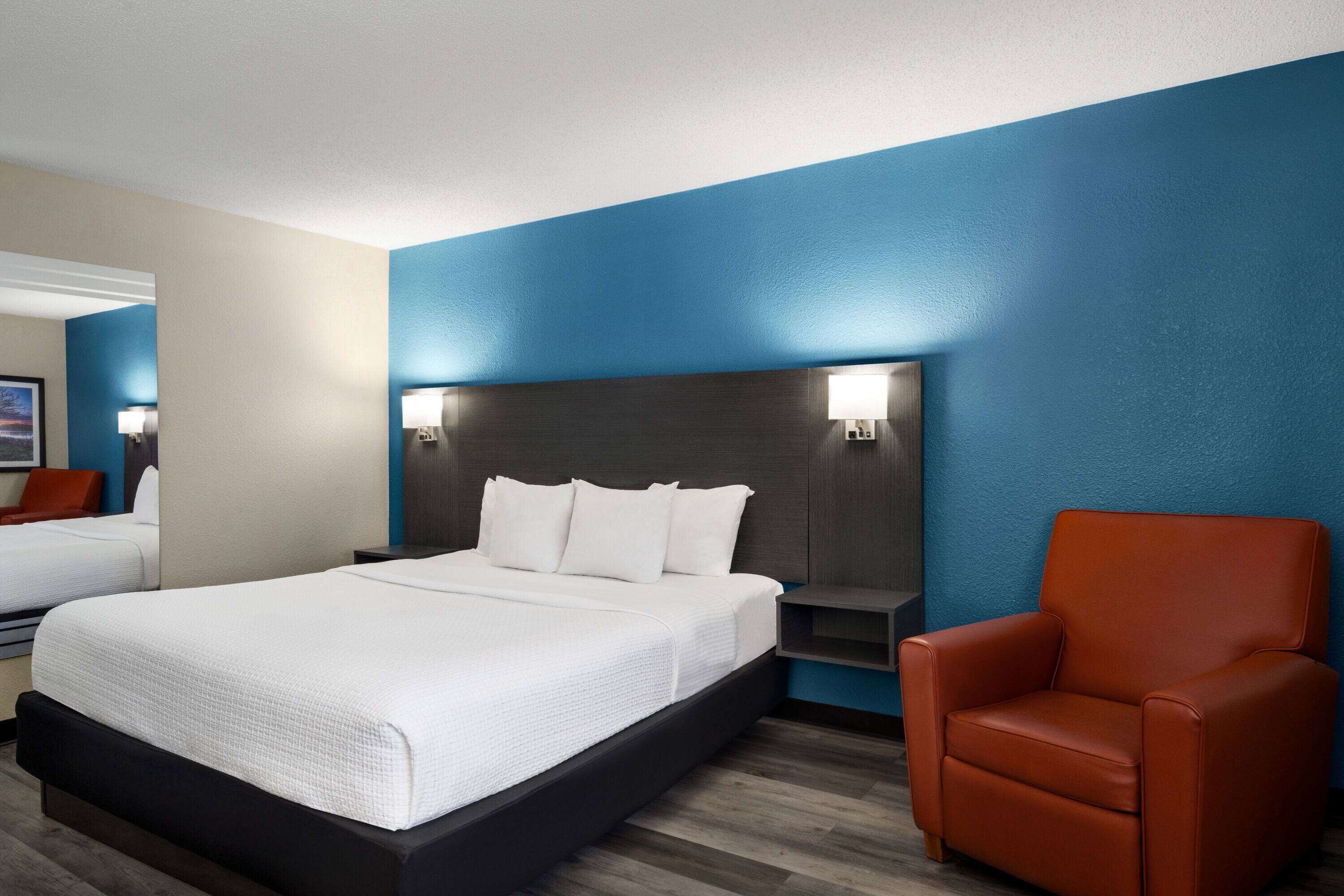 A hotel room with a large bed, a nightstand, a red armchair, and a blue accent wall.