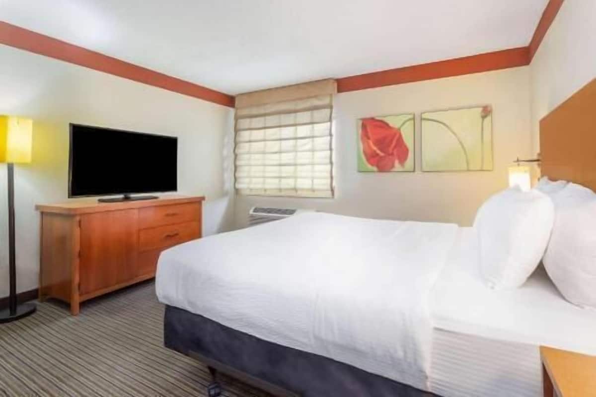 Una habitación de hotel con cama, televisión, escritorio y ventana con persianas.